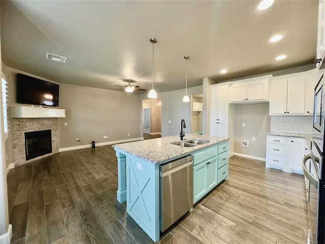 kitchen featuring stainless steel appliances, a sink, open floor plan, white cabinetry, and wood finished floors