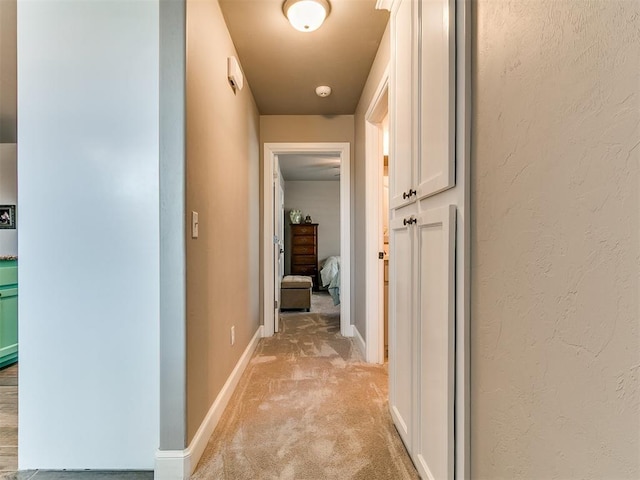 hallway with baseboards and light carpet