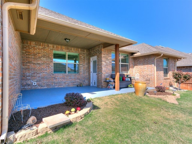 exterior space with brick siding, a lawn, a shingled roof, and a patio