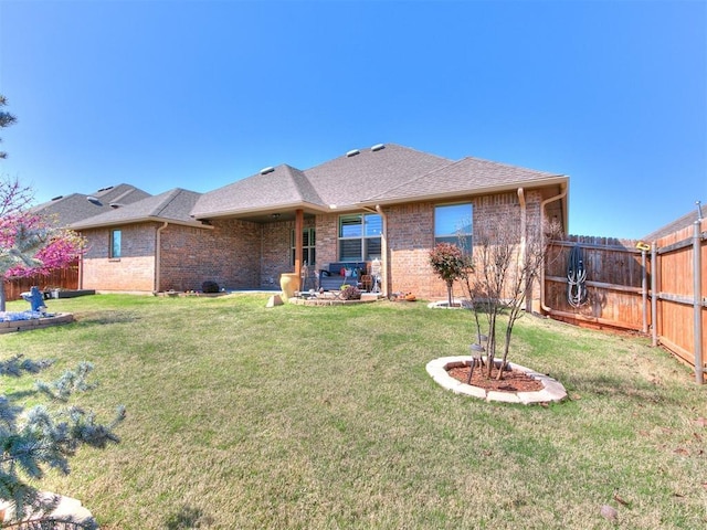 rear view of house featuring brick siding, a yard, a shingled roof, and a fenced backyard