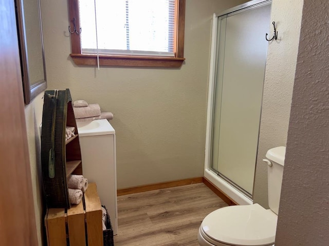 full bath featuring toilet, a stall shower, wood finished floors, and baseboards