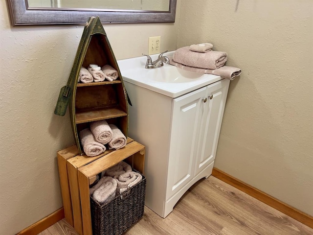bathroom featuring a textured wall, baseboards, vanity, and wood finished floors