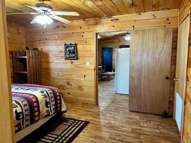 bedroom with wood walls, wooden ceiling, hardwood / wood-style flooring, and freestanding refrigerator