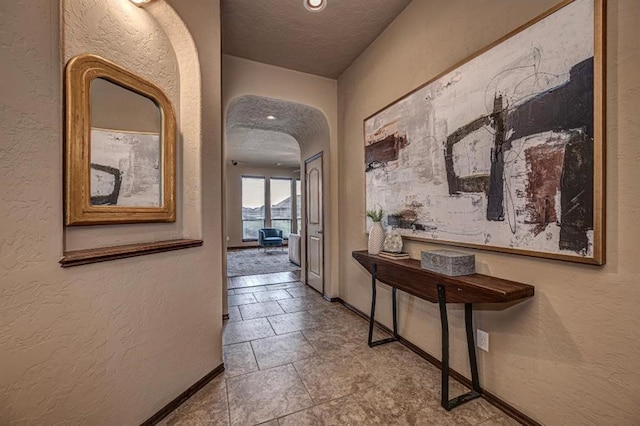 9609 Lakecrest Dr, Oklahoma City, OK 73159 - hallway featuring a textured wall, arched walkways, a textured ceiling, and baseboards