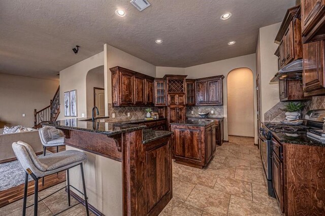 9609 Lakecrest Dr, Oklahoma City, OK 73159 - kitchen with visible vents, arched walkways, gas range, a peninsula, and under cabinet range hood