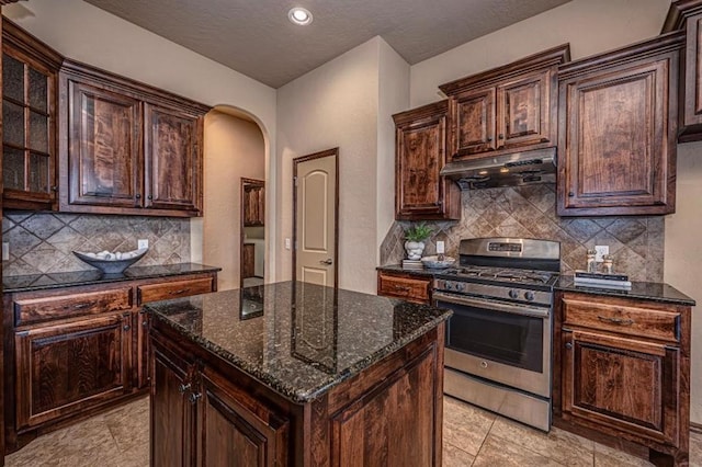 9609 Lakecrest Dr, Oklahoma City, OK 73159 - kitchen featuring a center island, arched walkways, under cabinet range hood, stainless steel gas stove, and dark stone counters