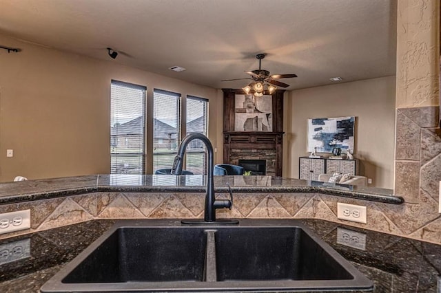 9609 Lakecrest Dr, Oklahoma City, OK 73159 - kitchen with dark stone countertops, ceiling fan, a sink, and a stone fireplace