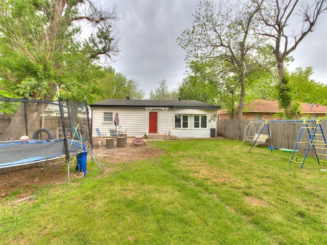 rear view of house featuring a playground, a fenced backyard, entry steps, a lawn, and a trampoline