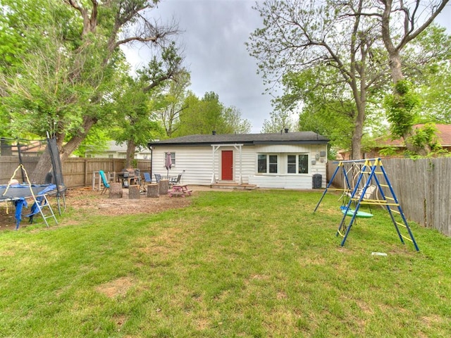 back of property with a lawn, a fenced backyard, an outdoor fire pit, and a trampoline