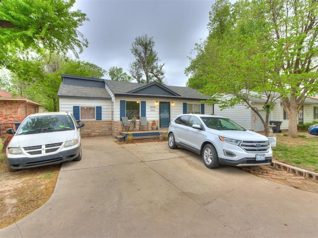 ranch-style house featuring concrete driveway, roof with shingles, and stone siding