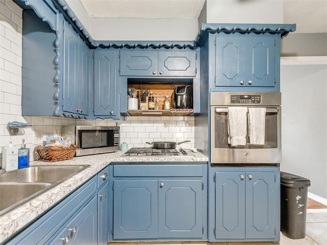 kitchen with blue cabinets, stainless steel appliances, a sink, and tasteful backsplash