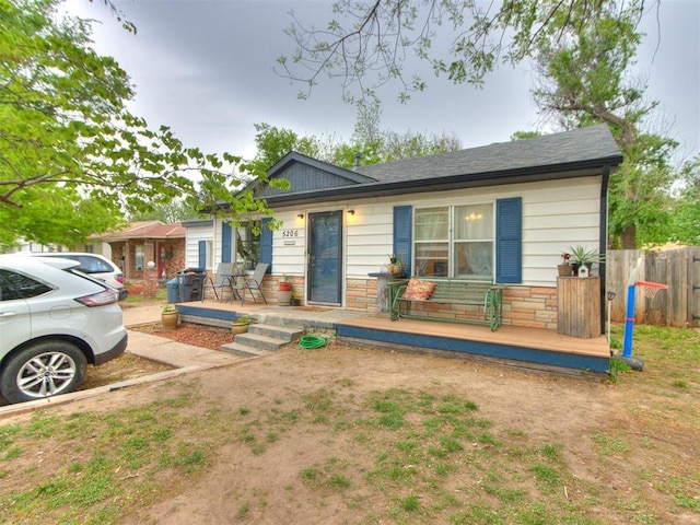 ranch-style house featuring covered porch, stone siding, and fence