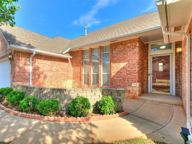 9333 SW 22nd St, Oklahoma City, OK 73128 - view of exterior entry with an attached garage, brick siding, and a shingled roof