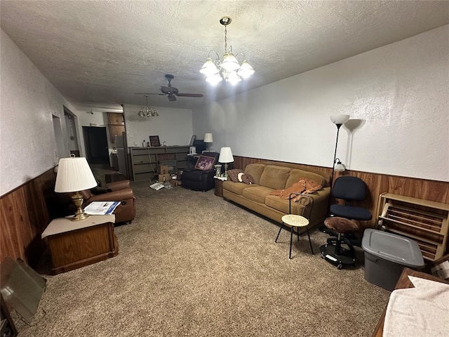 carpeted living area featuring a textured wall, a textured ceiling, wood walls, wainscoting, and ceiling fan with notable chandelier