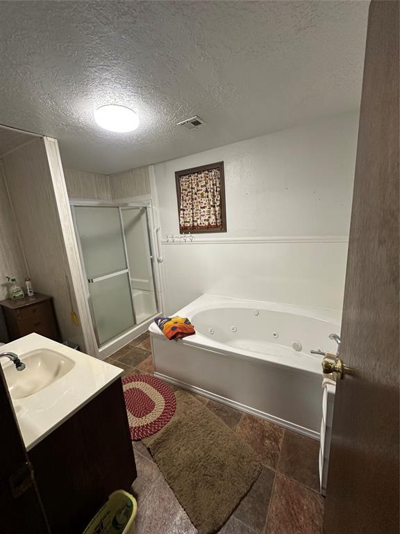full bathroom featuring a textured ceiling, vanity, visible vents, a whirlpool tub, and a stall shower