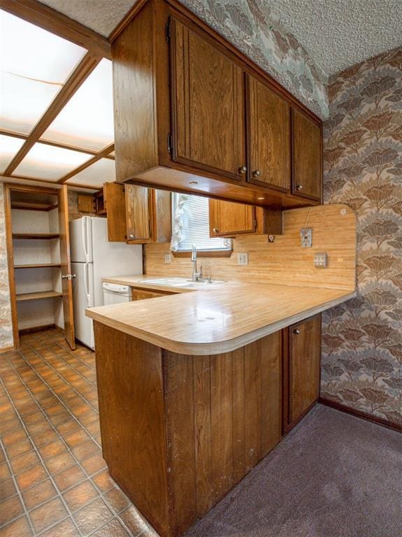 1520 NE 2nd St, Moore, OK 73160 - kitchen with wallpapered walls, brown cabinetry, a sink, a peninsula, and light countertops