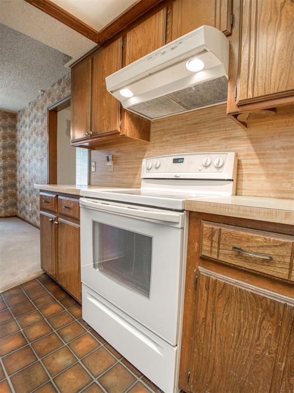 1520 NE 2nd St, Moore, OK 73160 - kitchen featuring brown cabinetry, under cabinet range hood, light countertops, electric range, and wallpapered walls