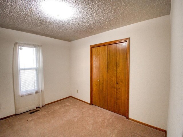 1520 NE 2nd St, Moore, OK 73160 - unfurnished bedroom with a closet, a textured ceiling, baseboards, visible vents, and light colored carpet