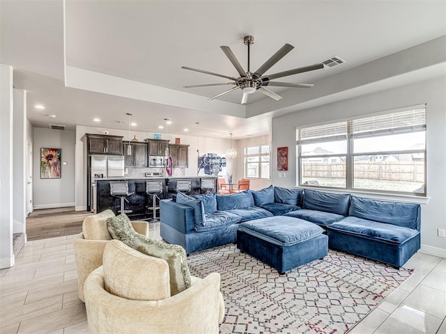 living area featuring ceiling fan, visible vents, recessed lighting, a raised ceiling, and baseboards