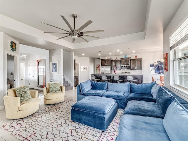 living area with a tray ceiling, a ceiling fan, recessed lighting, stairway, and light tile patterned flooring