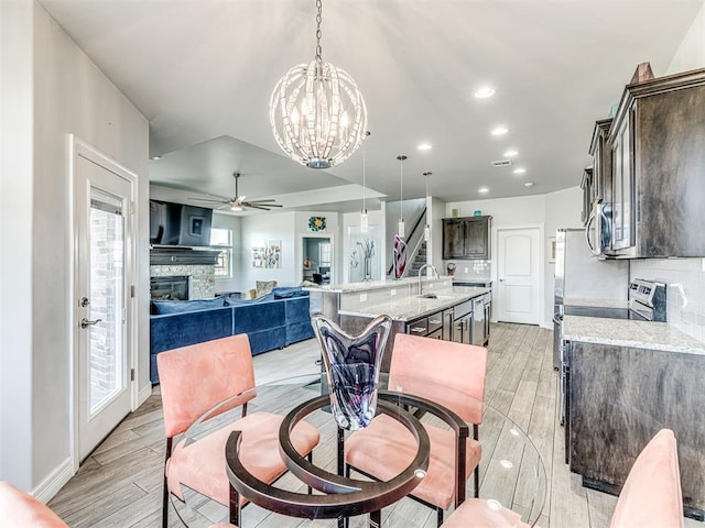 dining area with ceiling fan with notable chandelier, a stone fireplace, recessed lighting, wood tiled floor, and stairs