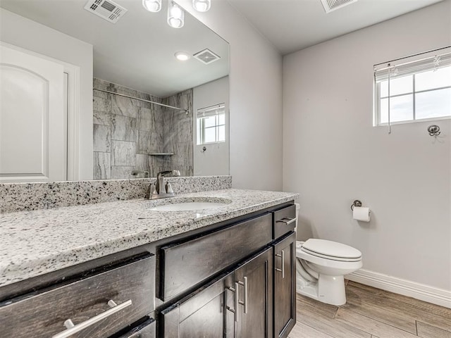 bathroom with a tile shower, wood finished floors, baseboards, and visible vents