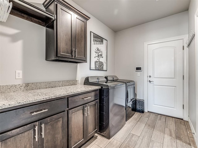 clothes washing area with light wood-style floors, washer and clothes dryer, and cabinet space