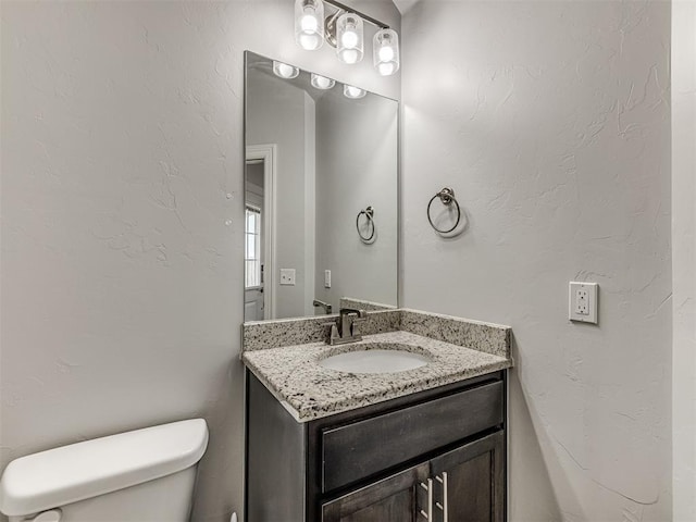 half bathroom with toilet, vanity, and a textured wall
