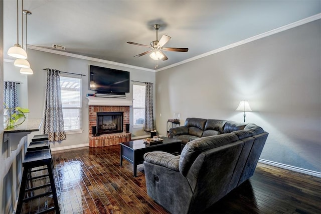 living area with baseboards, a brick fireplace, ornamental molding, ceiling fan, and dark wood-type flooring