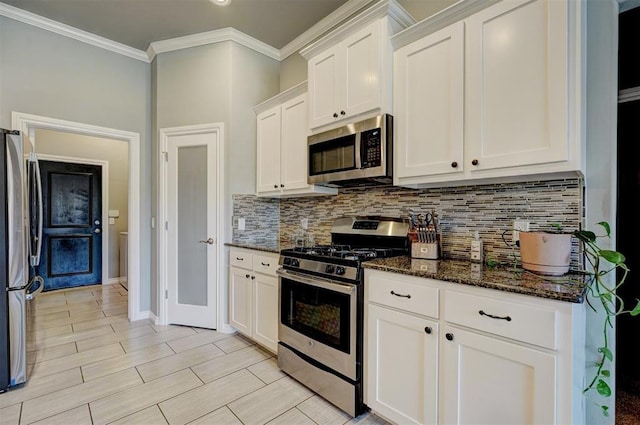 kitchen with ornamental molding, white cabinets, dark stone countertops, stainless steel appliances, and backsplash