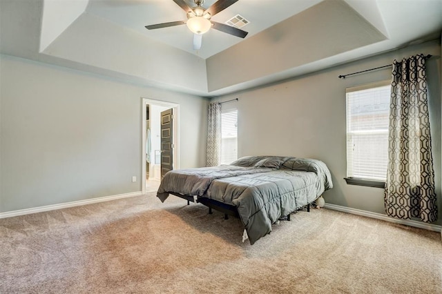 carpeted bedroom featuring a tray ceiling, baseboards, a ceiling fan, and visible vents