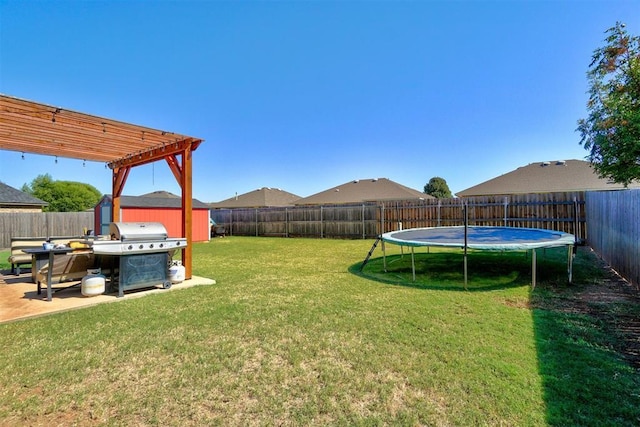 view of yard with a shed, a patio area, a trampoline, a fenced backyard, and an outbuilding