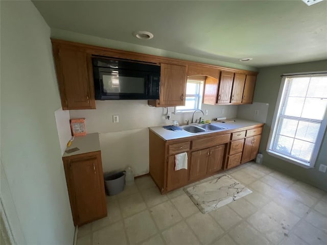 kitchen with brown cabinetry, light floors, a sink, and black microwave