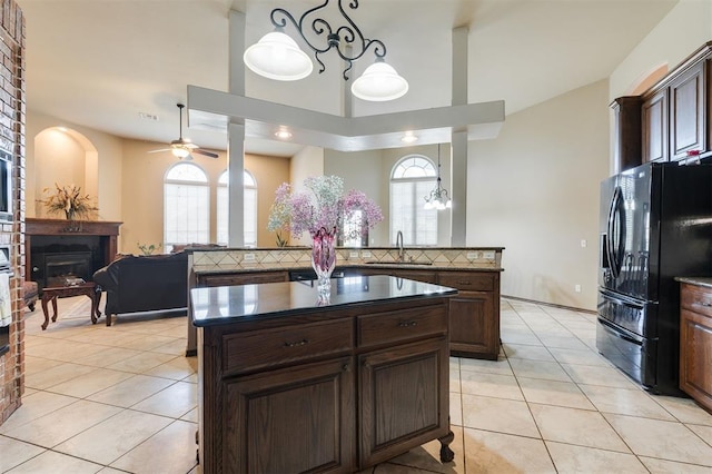 19605 Talavera Ln, Edmond, OK 73012 - kitchen featuring ceiling fan, a fireplace, a kitchen island, a sink, and black fridge with ice dispenser