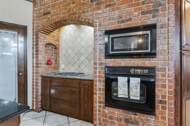 19605 Talavera Ln, Edmond, OK 73012 - kitchen with dark stone countertops, brick wall, light tile patterned floors, and stainless steel appliances