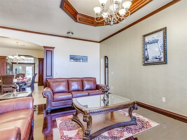 living area with a chandelier, arched walkways, a tray ceiling, wood finished floors, and crown molding