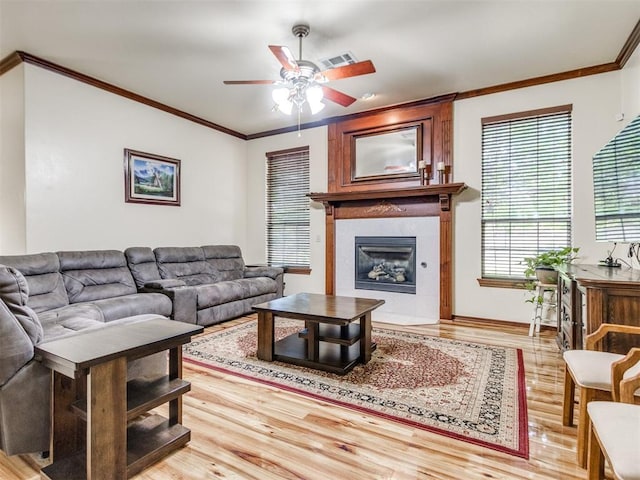 living area with ceiling fan, a glass covered fireplace, wood finished floors, and crown molding