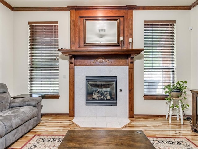 living area with light wood-style floors, a fireplace, ornamental molding, baseboards, and healthy amount of natural light