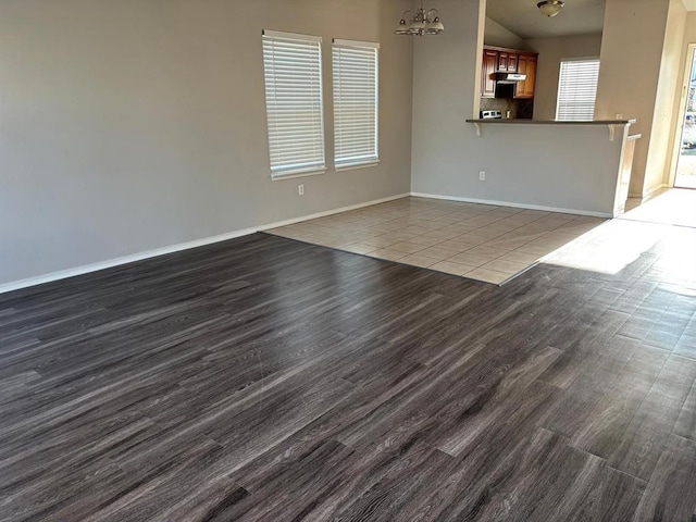 unfurnished living room featuring baseboards, dark wood finished floors, a chandelier, and vaulted ceiling