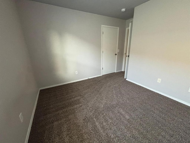 spare room with baseboards and dark colored carpet