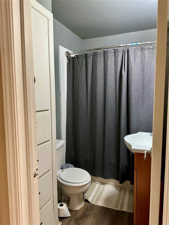 712 1st St, Maysville, OK 73057 - full bathroom featuring wood finished floors, toilet, and a shower with curtain