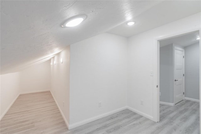 below grade area with baseboards, light wood-style floors, and a textured ceiling