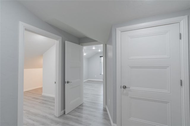 hall featuring baseboards, light wood finished floors, and lofted ceiling
