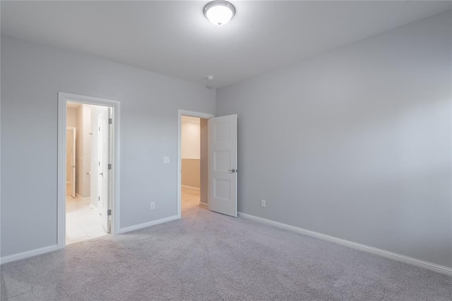 unfurnished bedroom with baseboards, ensuite bath, and light carpet