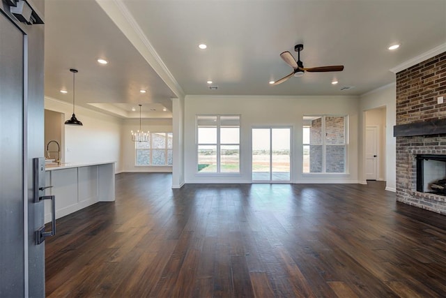 unfurnished living room featuring a wealth of natural light, a brick fireplace, ceiling fan with notable chandelier, and dark wood finished floors