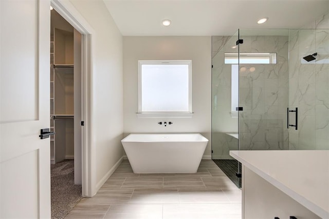 bathroom featuring a marble finish shower, a spacious closet, a freestanding bath, and baseboards