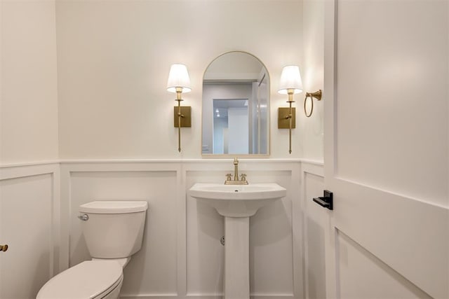 bathroom with a decorative wall, toilet, a wainscoted wall, and a sink