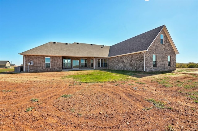 back of property with a yard, a shingled roof, central AC unit, and brick siding