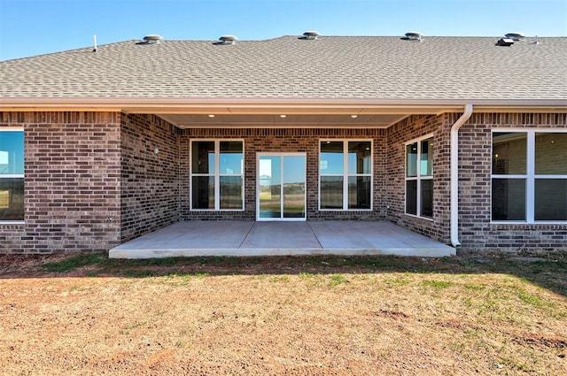 back of property with brick siding, a shingled roof, and a patio