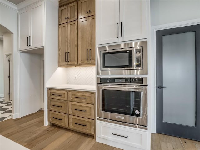 kitchen with tasteful backsplash, light wood-style flooring, light countertops, appliances with stainless steel finishes, and arched walkways
